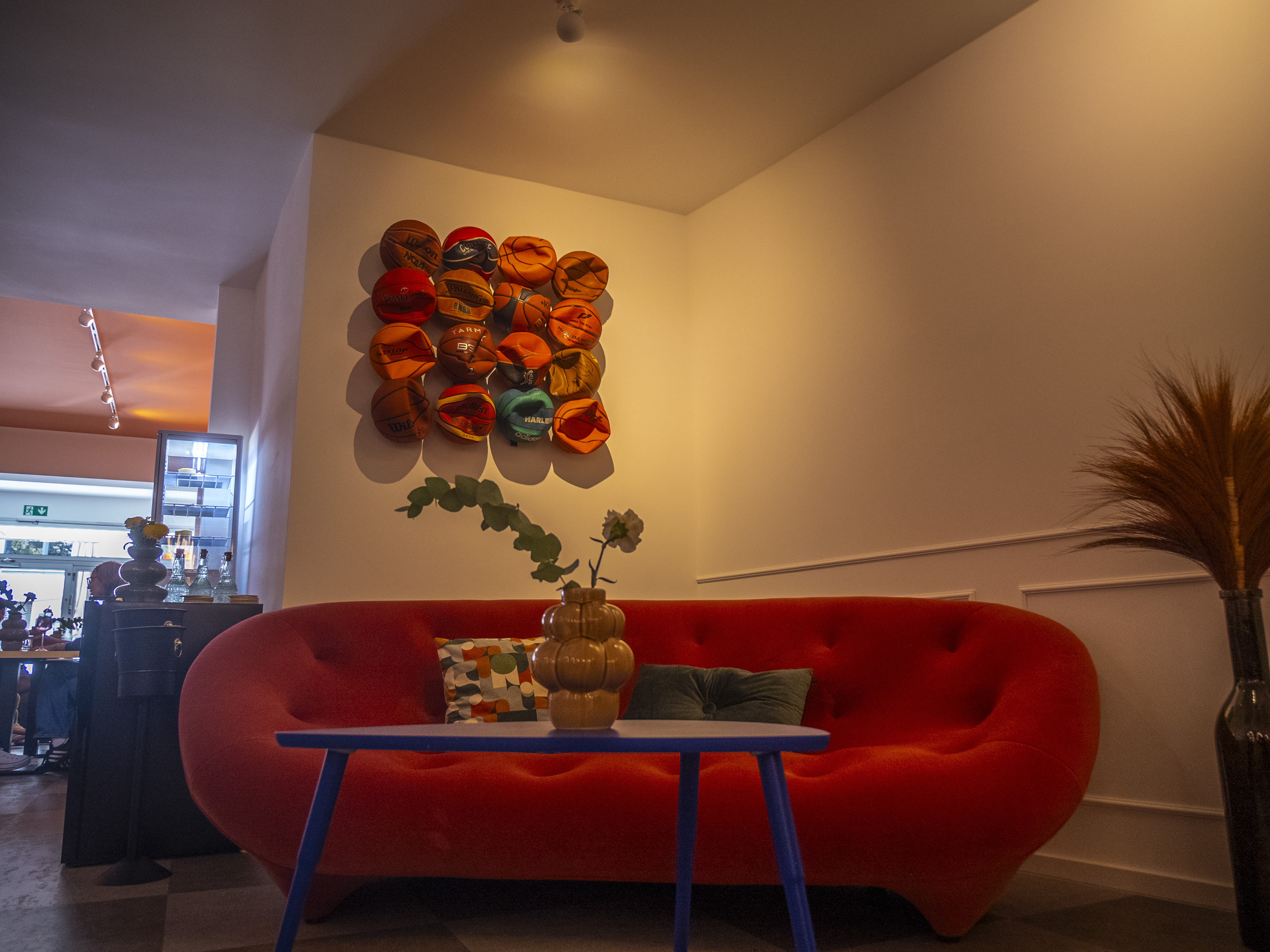 Joo_Bene_Fotos_15 Ein rundes Stoffsofa steht in einer Zimmerecke mit roter Wanddeko.