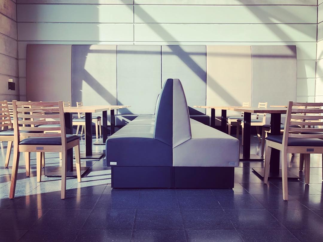 Sonnenlicht erhellt eine Kantine mit Lederbänken und Holzstühlen und -tischen.